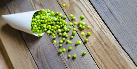 Tasty, green, fresh peas in a paper bag on a wooden background. Peeled green peas fall out of the bag. Wood background. Close-up. Copy spaceの写真素材