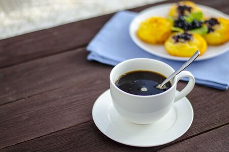 On the dish are three cheesecakes with blueberries and one without toppings, garnished with fresh blueberries and mint leaves. Composition on a textile napkin with a cup of coffee. Close-up. Copy space.の写真素材