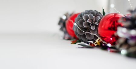 Close-up Christmas composition of balls, pine cones and garlands on a white background. Pine cones and red balls are located diagonally on the right side of the background, confetti lie randomly. Copy spaceの写真素材