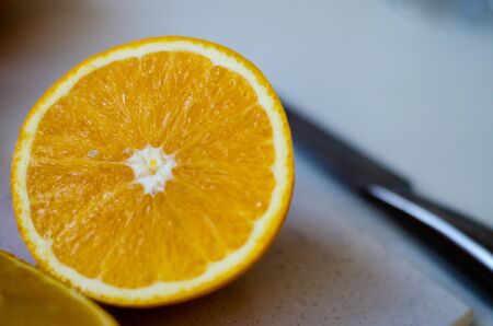 On a wooden table lies a stone board and a knife. An orange is cut in half on a board. The concept of a healthy diet, natural fruits, juices, smoothies. Close-up. Copy spaceの写真素材