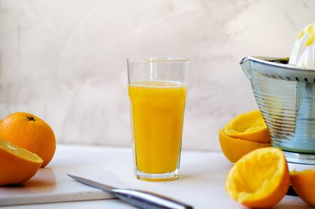 On a wooden table, one whole orange, one cut in half, peel of an orange. On the table lies a stone board and a knife. In the background is a glass cup with freshly squeezed orange juice. On the right side is a citrus juice squeezer. The concept of a healthy diet, natural fruits, juices, smoothies. Copy spaceの写真素材