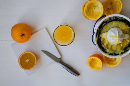 On a wooden table, one whole orange, one cut in half, peel of an orange. On the table lies a stone board and a knife. In the background is a glass cup with freshly squeezed orange juice. On the right side is a citrus juice squeezer. The concept of a healthy diet, natural fruits, juices, smoothies. Top veiw. Copy spaceの写真素材