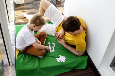Happiness in the details A young father plays board games, dominoes with his son. On a cozy and comfortable balcony, dad and son play on a sunny weekend. Slow life, slow down time when with family. Top view. Close-up.の写真素材