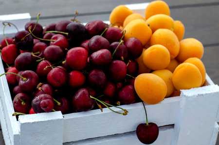 Fresh apricots and cherries in a white wooden box. Half apricots, half cherries. Vegetarian food,...
