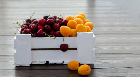 Fresh apricots and cherries in a white wooden box. Half apricots, half cherries. Vegetarian food, supplies. Sale in private gardens. Vitamins Close-up. Copy space.の写真素材