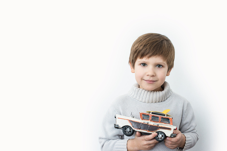 boy in a sweater holding a toy retro car on a white backgroundの写真素材
