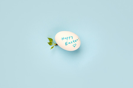 happy easter egg and branch with young leaves on blue backgroundの写真素材
