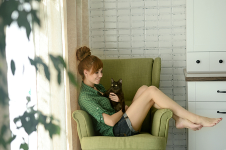 girl in home clothes sitting in a chair with a cat in her armsの写真素材