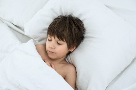 sleeping child, boy lies in a bed on a white bedclothes. Top view. European childの写真素材