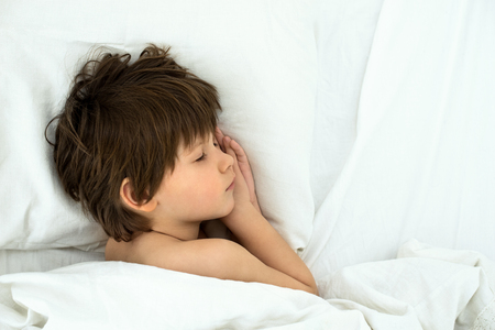 sleeping child, boy lies in a bed on a white bedclothes. Top view. European childの写真素材