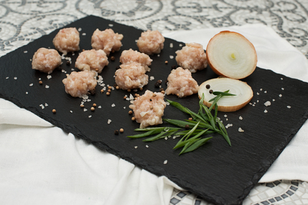 ingredients for making soup with meatballs. raw meat, onions and noodles on a black stone boardの写真素材