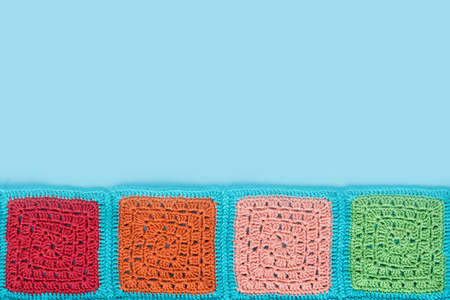 crocheted  lace tablecloth of multicolored squares ornament on a blue background, top view, place for text, natural wool.の写真素材