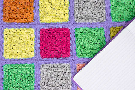 crocheted  lace tablecloth of multicolored squares ornament, sheet of notebook to write to the ruler, top view, place for text, natural wool.の写真素材