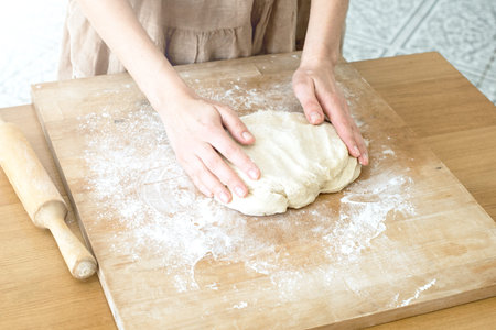 female hands knead the dough on a wooden board cooking baking
