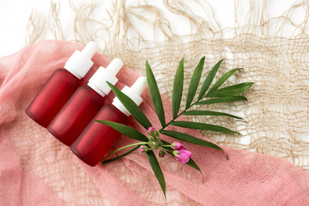 pink bottles for cosmetics, oil, on the background of natural burlap and green palm twigの写真素材
