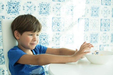 a boy in a blue T-shirt has breakfast with oatmeal and milk. cereal in a white plate, space for...