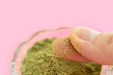 natural henna powder and white flower in a female hand on a pink background. Concept female beauty and cosmetology. Eyebrow and hair coloring.の写真素材