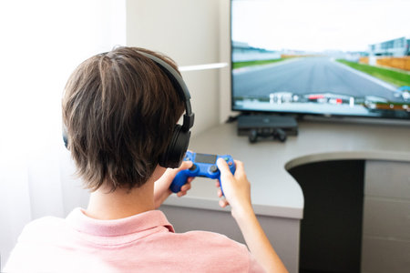Teenager boy online plays a computer game with headphones and a joystick, game console.