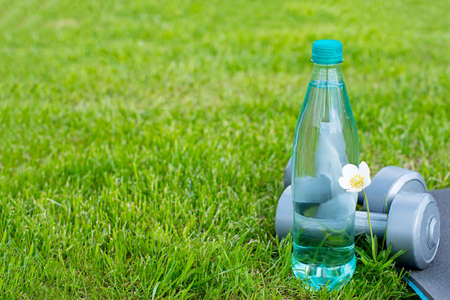 Bottle with water, dumbbells and a mat for sports and yoga on the green grass. Copy spaceの写真素材
