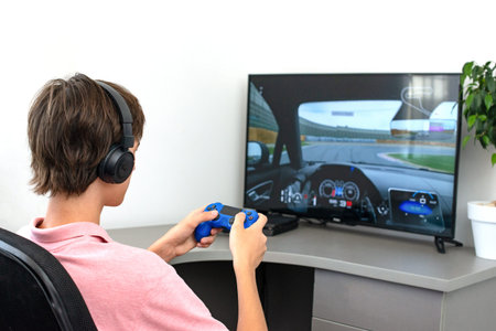 Teenager boy online plays a computer game with headphones and a joystick, game console.
