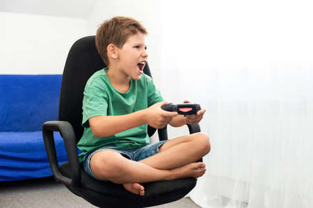 Teenager boy online plays a computer game with headphones and a joystick, game console.の写真素材