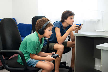 Teenager boy online plays a computer game with headphones and a joystick, game console.の写真素材