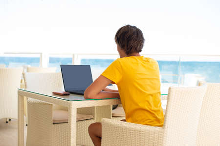 Workplace in a cafe with a sea view. Man working on a laptop in a cafe. Copy space, Mock up.の写真素材