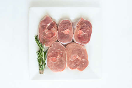 pieces of raw turkey meat, chopped leg steak, portioned barbecue pieces, on a round wooden board and and a white background with a sprig of rosemary, tomatoes and red hot pepper. isolate ...の写真素材