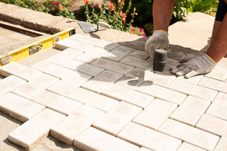 The master lays paving stones in layers. Garden brick pathway paving by professional paver worker. Laying gray concrete paving slabs in house courtyard on sand foundation base.の写真素材