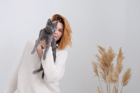 The red hair woman holds the gray cat in hands. neutral colors. verticalの写真素材