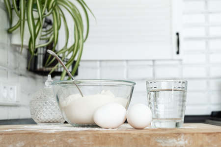 Pouring Water into Flour. Making dough by female hands in white moden kitchen in Scandinavian stile. eggs, flour and waterの写真素材