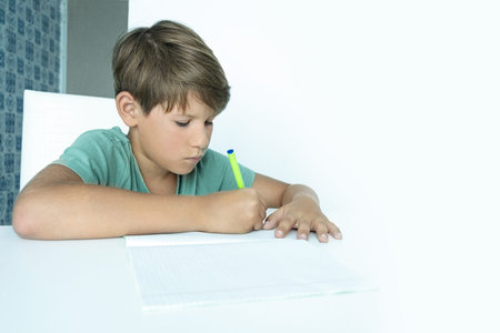 Sad boy with book does school homework. Back to school. Unhappy schoolboy with textbooks. Distance...