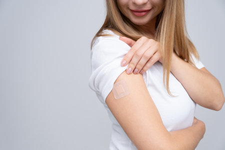 Young beautiful smiling real middle age woman in face mask and white T-shirt and glasses with a plaster on her hand rejoices from receiving a vaccination against virus infection. copy spaceの写真素材