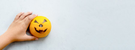 The hands of a boy drawing a scary muzzle on a pumpkin for the holiday of halloween. Minimalism. Gray and orangeの写真素材
