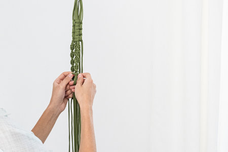 handmade green macrame plant hangers with potted plant are hanging on woman hand. The macrame have...