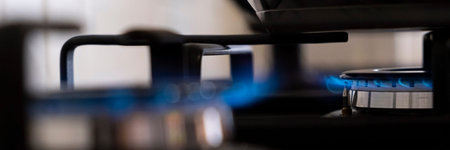 Close up of Burning gas burner with blue flames on kitchen black gas stove with a bokeh effect. Dark...