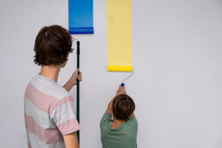 children paint the wall with a roller. teenagers spend time together helping to make repairs. Colors of Ukraine flag. Blue and yellowの写真素材