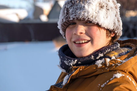 Portrait of smiling cute teenage boy, preteen playing in snow, in a snow-covered hat in winter...