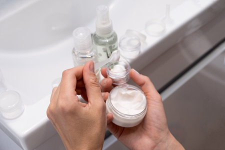 Filling a set of mini travel jars with cosmetics and care products in transparent travel bagの写真素材