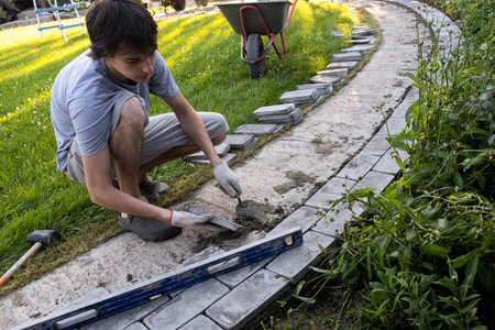Laying paving stones on cement mortar. Laying a garden path made of tiles. Self-laying of concrete paving slabs in the courtyard of the house. do it yourself. DIY. Spatula, level, malletの写真素材