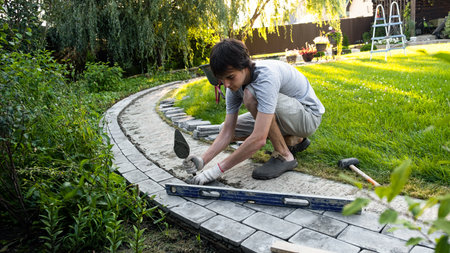 Laying paving stones on cement mortar. Laying a garden path made of tiles. Self-laying of concrete paving slabs in the courtyard of the house. do it yourself. DIY. Spatula, level, malletの写真素材