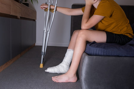 Teenager boy with injured broken leg in a plaster cast on the bed at home with crutches.の写真素材