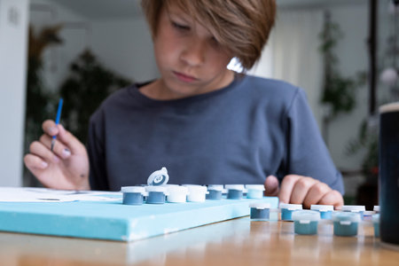 A boy, of European appearance, with long dark hair, draws a picture by numbers. children's passion...