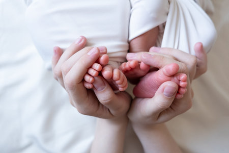 Mom and dad hands hold small legs of their two newborn twin babies.