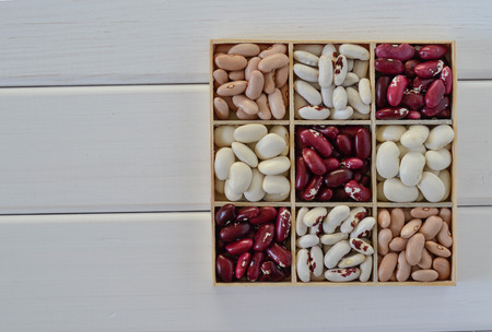Assortment of beans in wooden box on white wooden backgroundの写真素材
