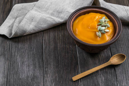 Pumpkin cream soup with seeds  in a clay bowl on dark wooden  tableの写真素材