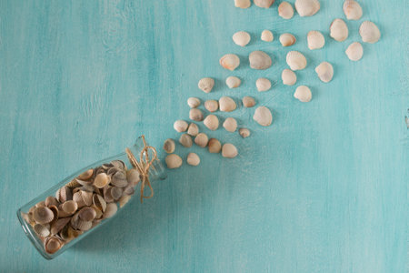 Seashells spill out of the bottle glass on the blue background. Top view