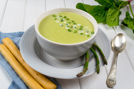Green spring pureed cream asparagus soup in ceramic bowl on white wooden tableの写真素材