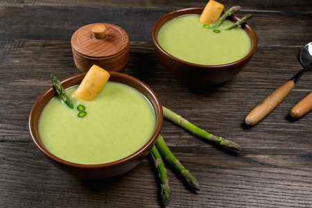 Green spring pureed  cream asparagus soup in ceramic bowl on dark wooden tableの写真素材