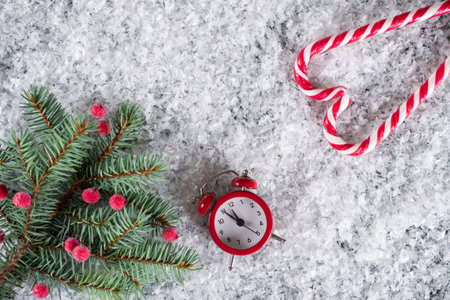 Christmas fir tree with decoration candy canes and red clock. On snow background.